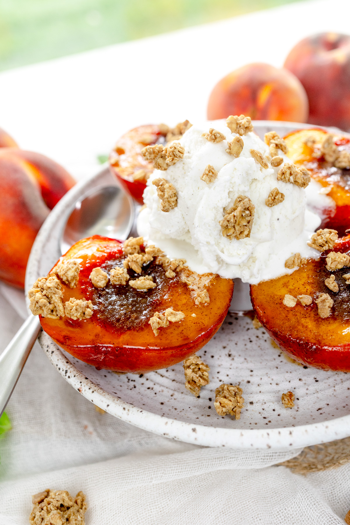 Close up image of Air Fryer Peaches on a white plate with a scoop of ice cream and crumb sprinkling on top, and a spoon.