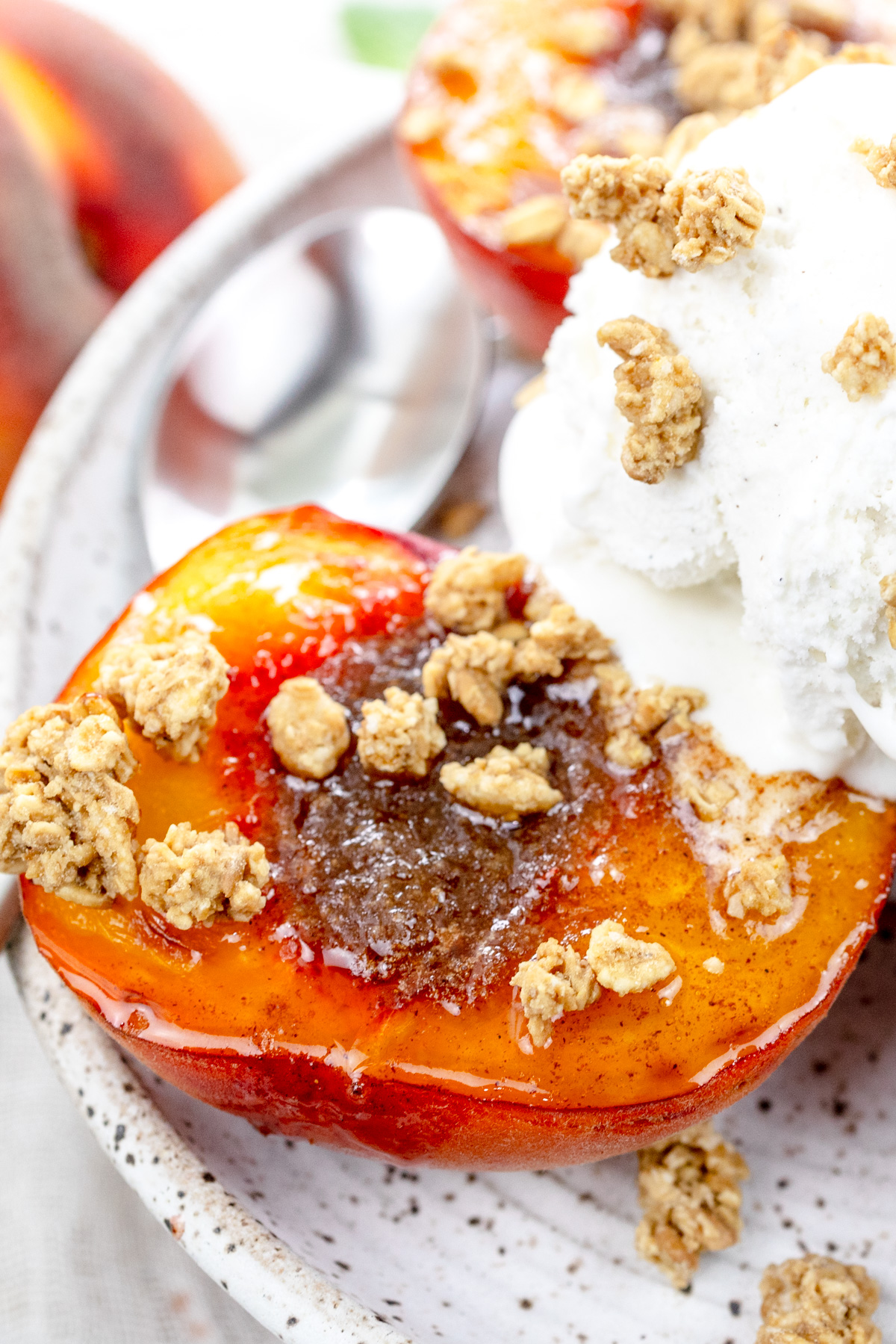 Close up image of Air Fryer Peaches on a white plate with a scoop of ice cream and crumb sprinkling on top, and a spoon.
