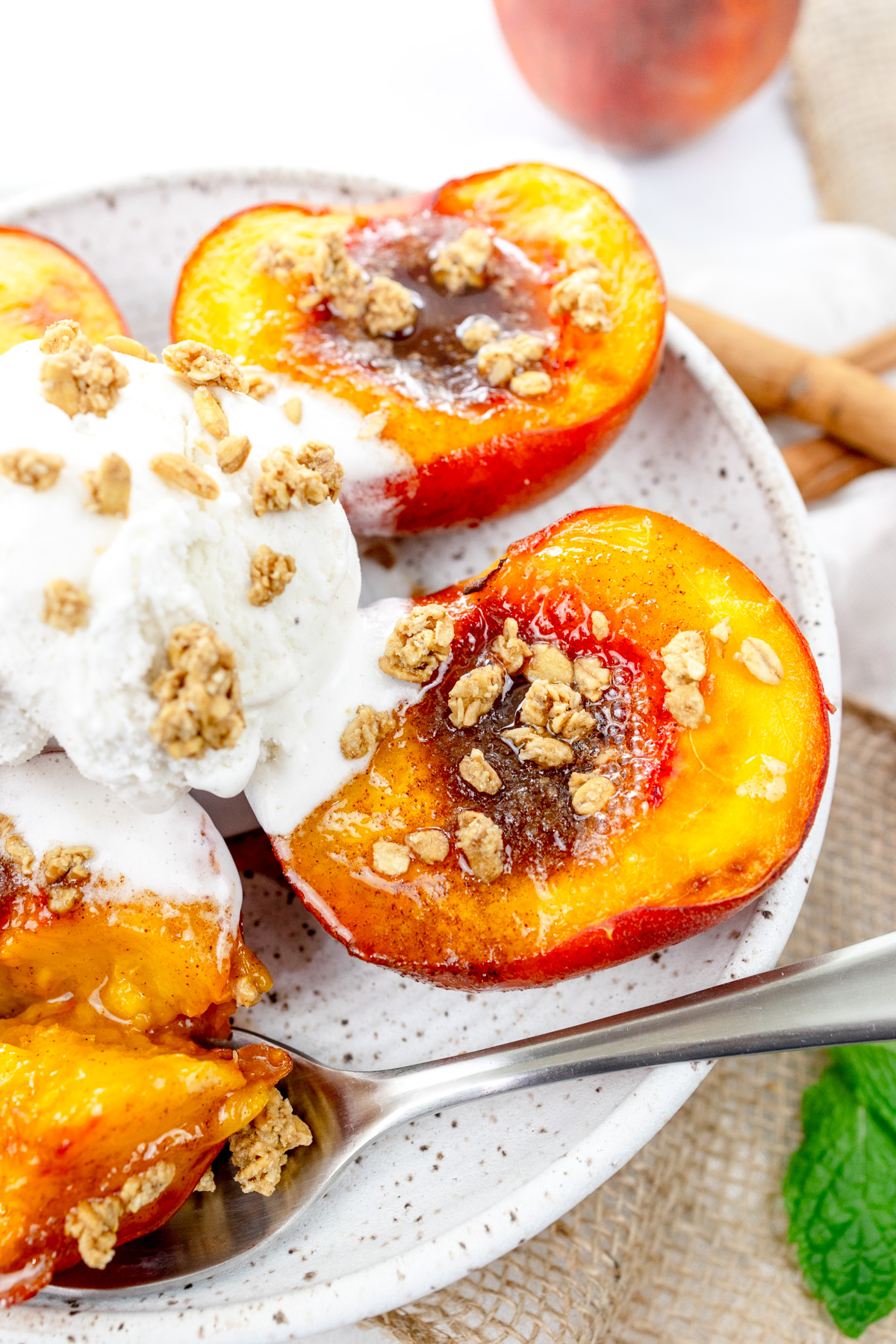 Close up image of Air Fryer Peaches on a white plate with a scoop of ice cream and crumb sprinkling on top, and a spoon.