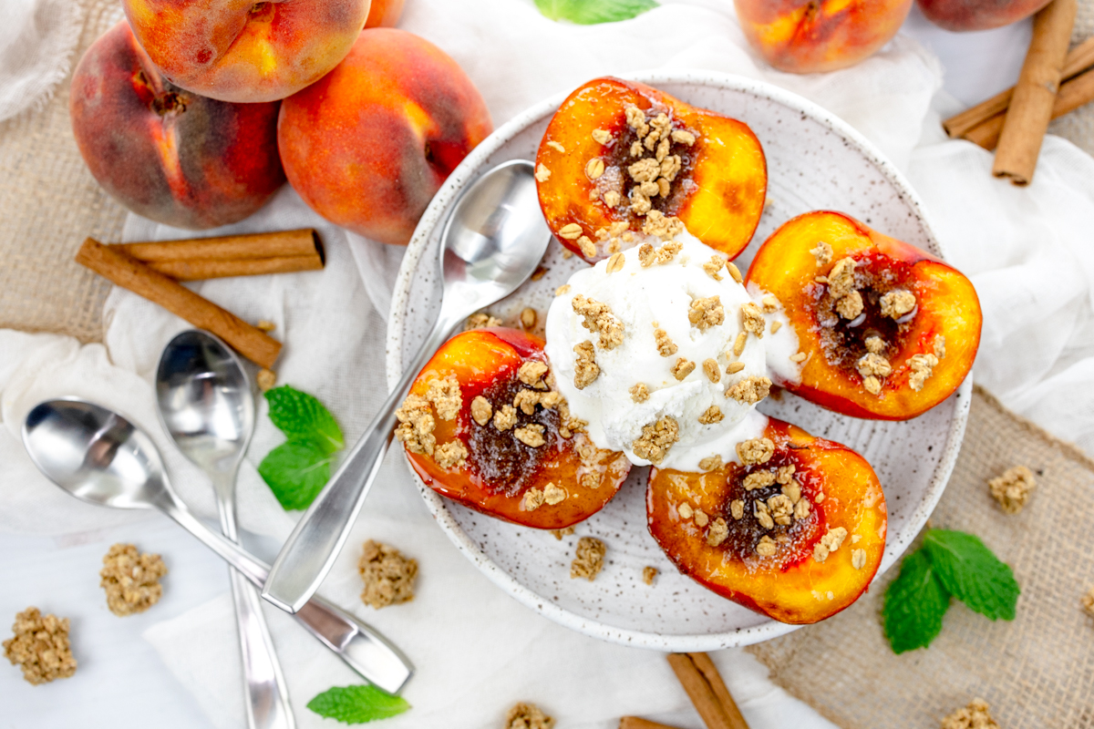 Overhead image of Air Fryer Peaches on a white plate with a scoop of ice cream and crumb sprinkling on top, and a spoon.