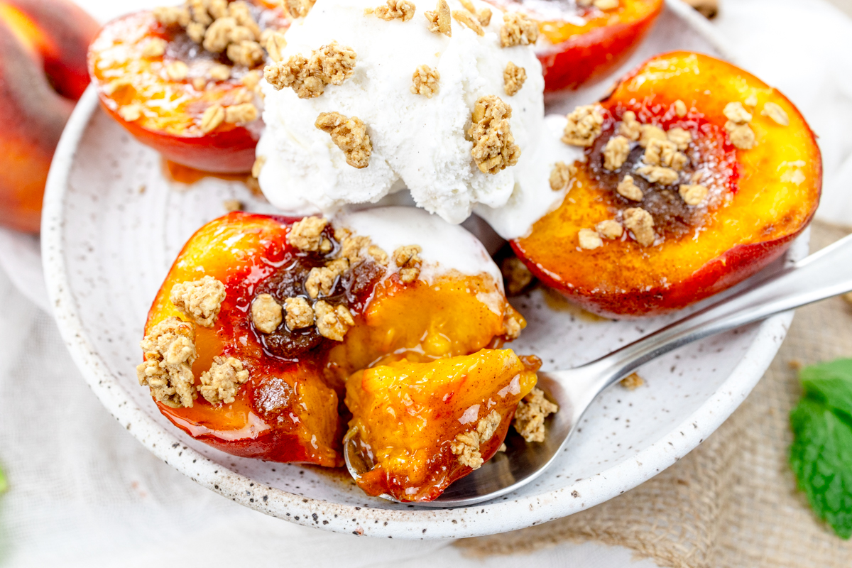 Close up image of Air Fryer Peaches on a white plate with a scoop of ice cream and crumb sprinkling on top, and a spoon.