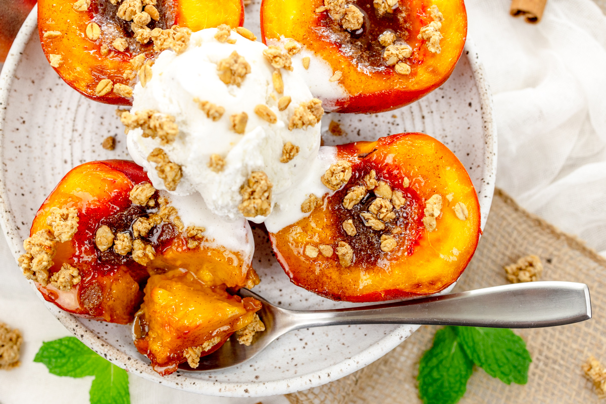 Overhead image of Air Fryer Peaches on a white plate with a scoop of ice cream and crumb sprinkling on top, and a spoon.