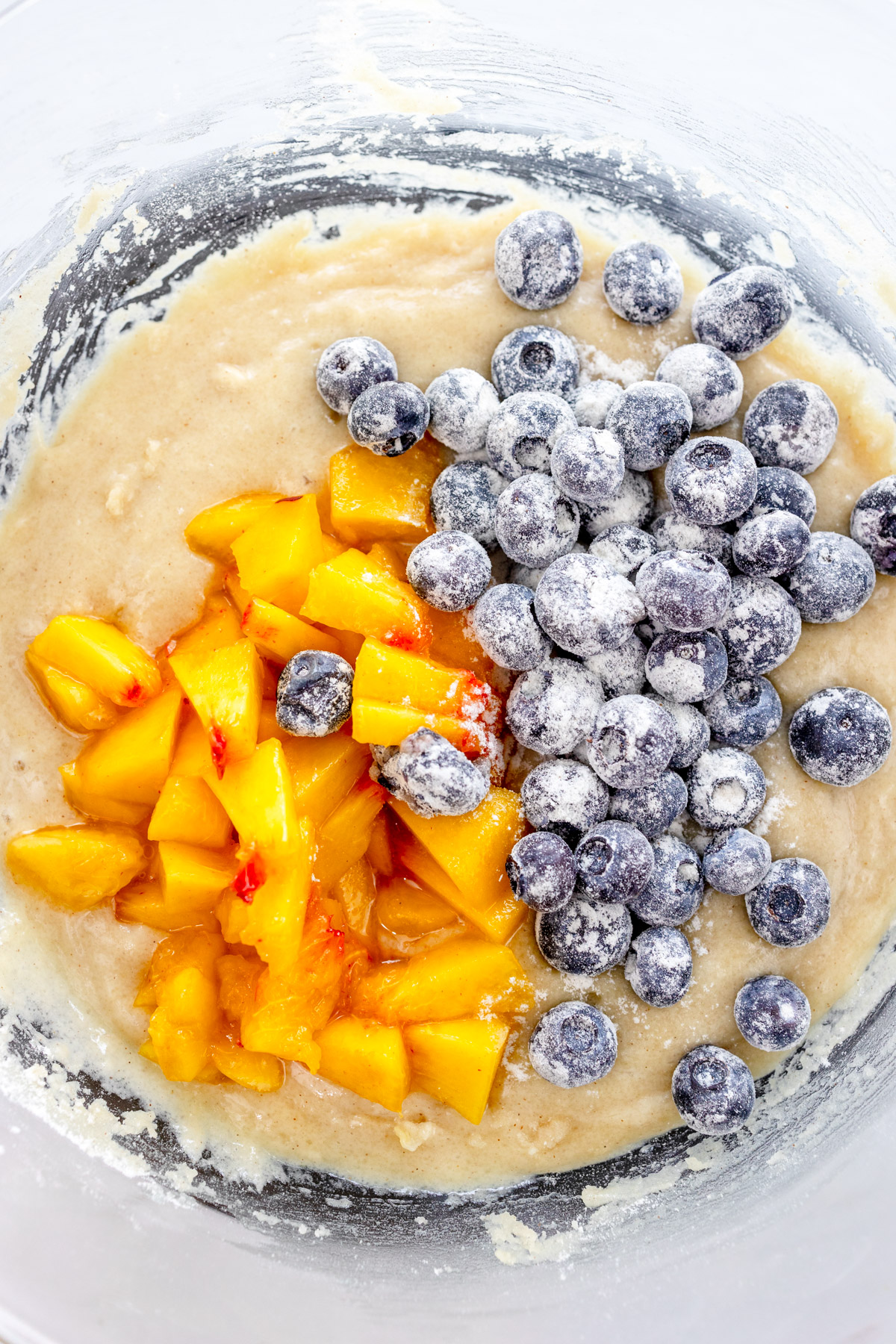 Overhead image of blueberries and peaches being added to Blueberry Peach Muffin batter.