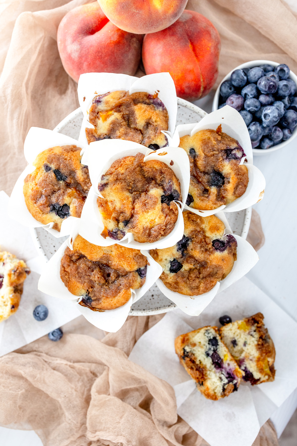 Overhead image of Blueberry Peach Muffins on a grey plate, surrounded by peaches and blueberries.