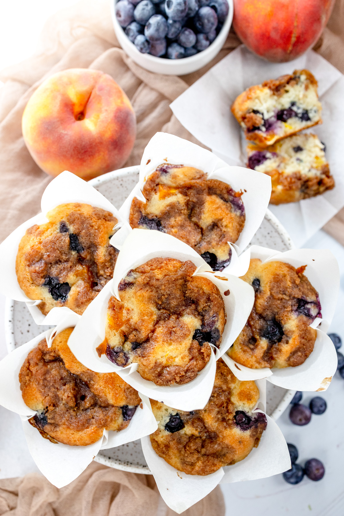 Overhead image of Blueberry Peach Muffins on a grey plate, surrounded by peaches and blueberries.