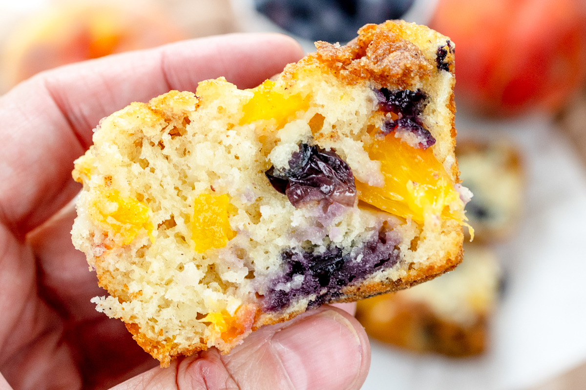 Close up image of a hand holding a Blueberry Peach Muffin that has been cut in half.