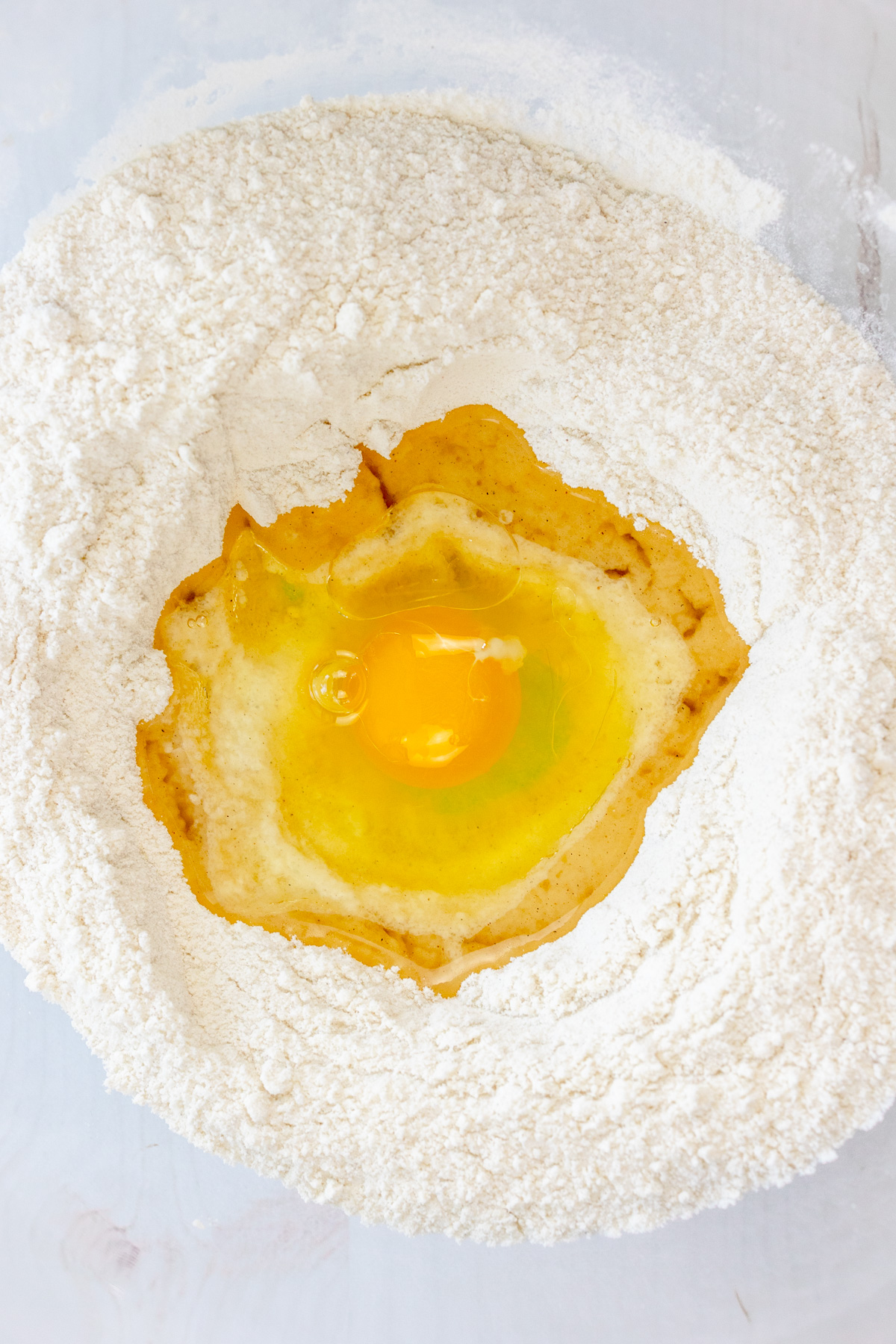 Close up image of a mixing bowl with dry ingredients needed for Cardamom Muffins, with an egg on top.