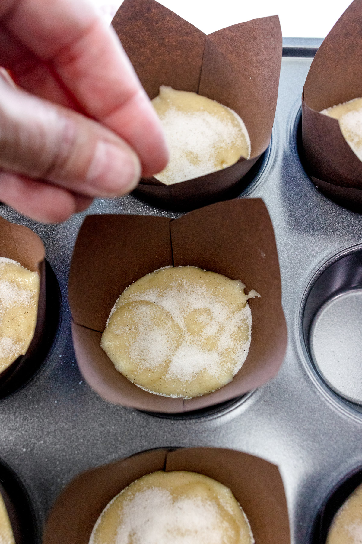 Close up image of a hand sprinkling the sugar and cardamom topping over a muffin.