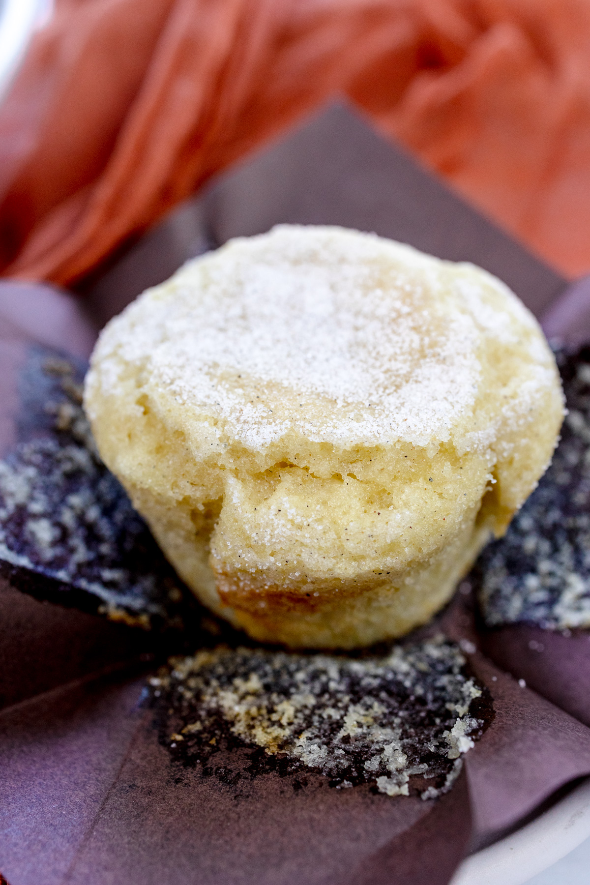 Close up image of a cardamom muffin on a brown, paper, unfolded paper muffin casing.