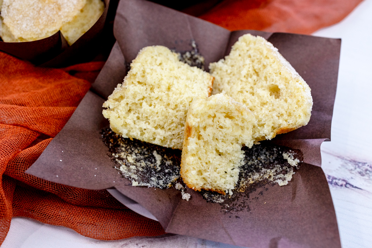Image of a Cardamom Muffin broken into three pieces, on an unfolded, brown paper muffin casing.
