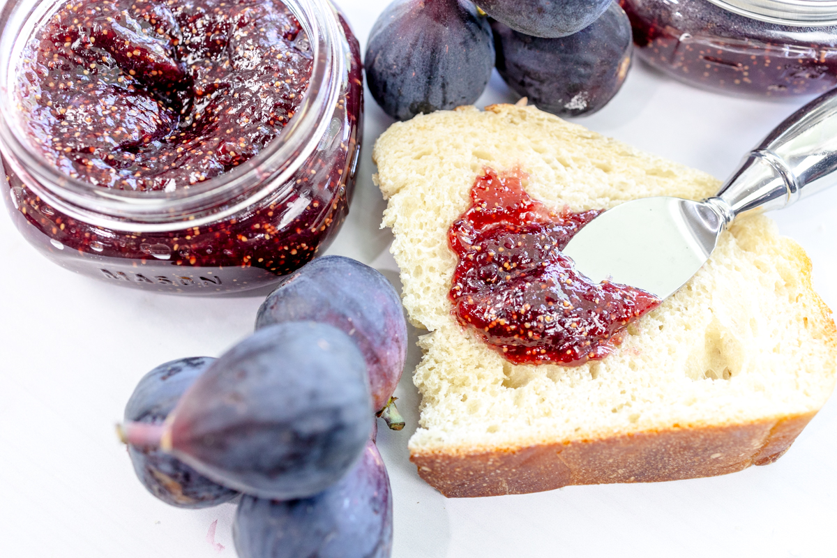 Fig Jam being spread on white bread, next to fresh figs.
