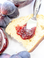 Fig Jam being spread on white bread, next to fresh figs.