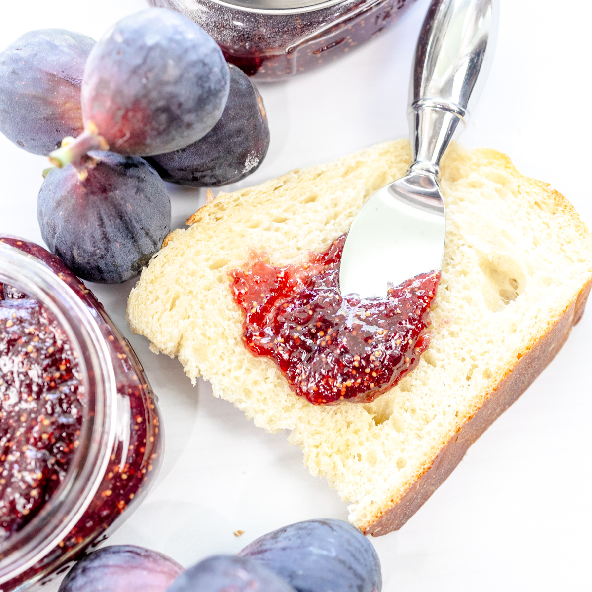 Fig Jam being spread on white bread, next to fresh figs.