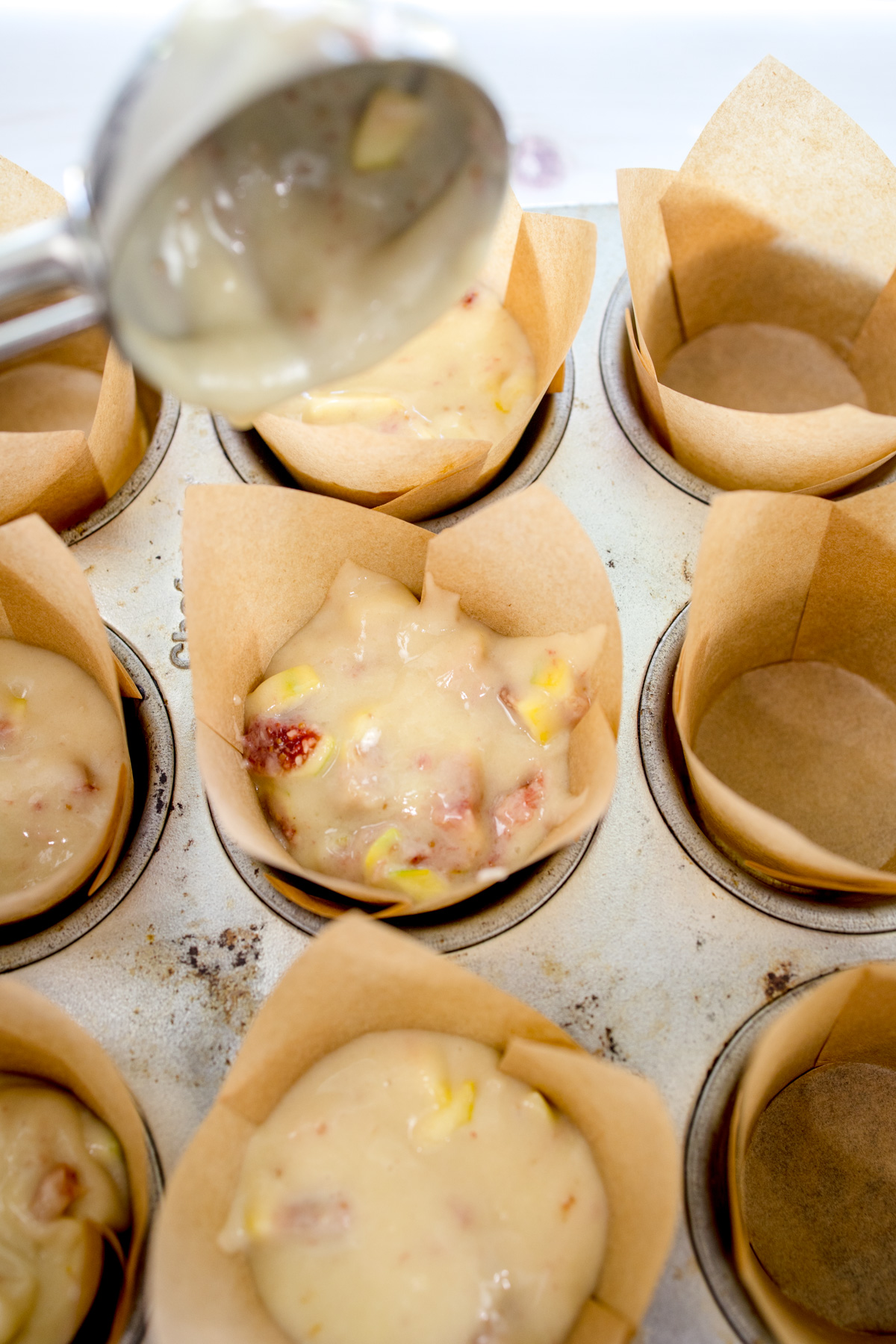Overhead image of fig muffin batter being spooned into muffin cases in a muffin tin.