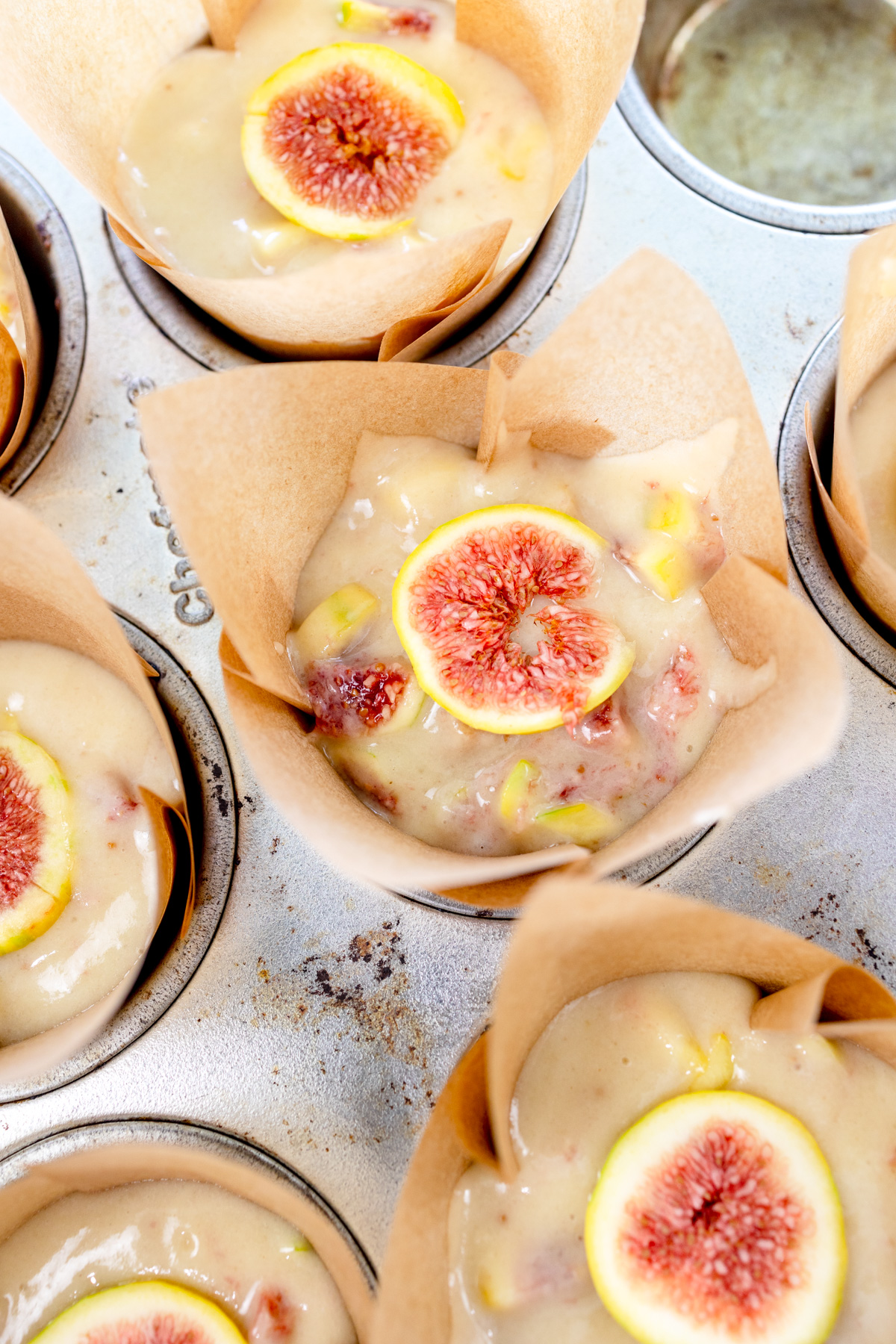 Close up image of fig muffin batter in muffin cases in a muffin tin a slice of fig on top.