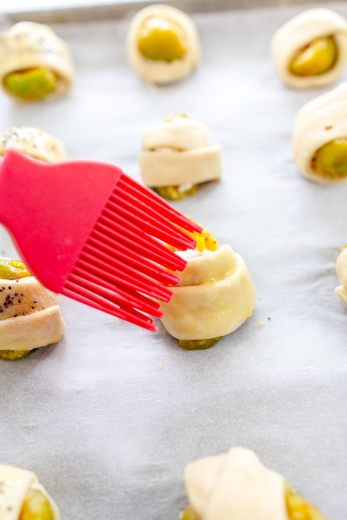Close up image of unbaked Figs in a Blanket being brushed with egg wash.