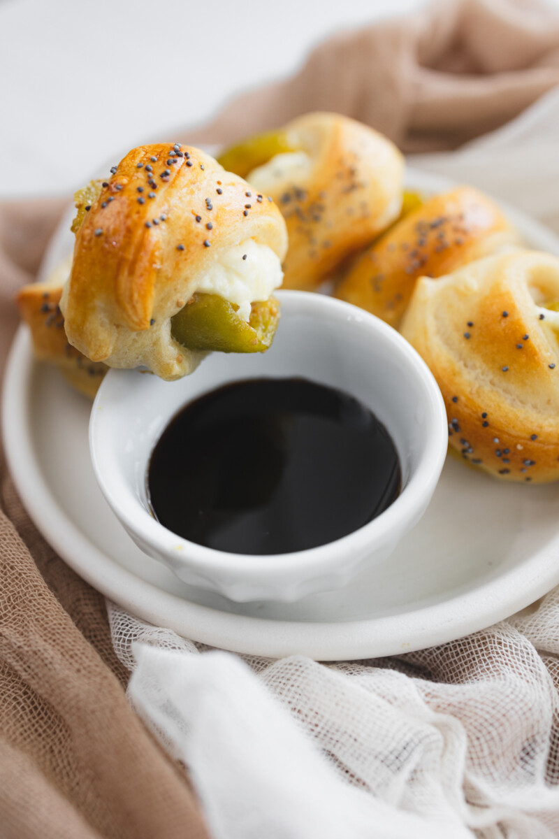 Close up image of Figs in a Blanket on a white plate next to a balsamic glaze dip.