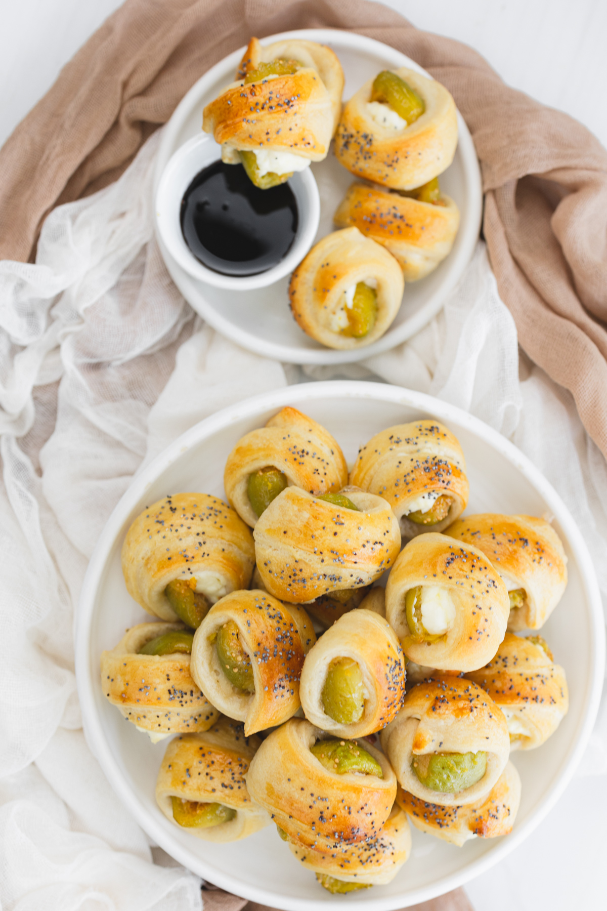 Overhead image of Figs in a Blanket on a white plate next to a smaller plate with Figs in Blankets and a balsamic glaze dip.