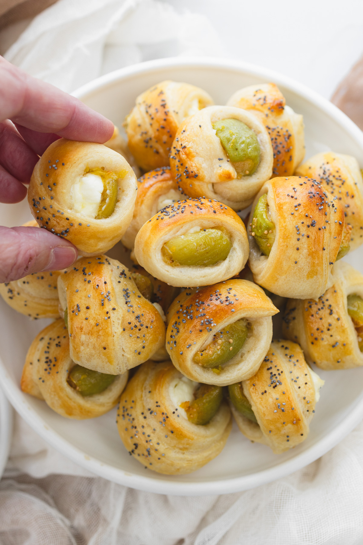 Overhead image of Figs in a Blanket on a white plate with a hand picking one up.