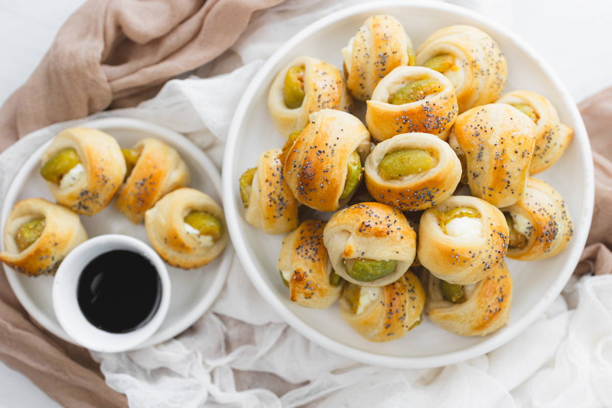 Overhead image of Figs in a Blanket on a white plate next to a smaller plate with Figs in Blankets and a balsamic glaze dip.