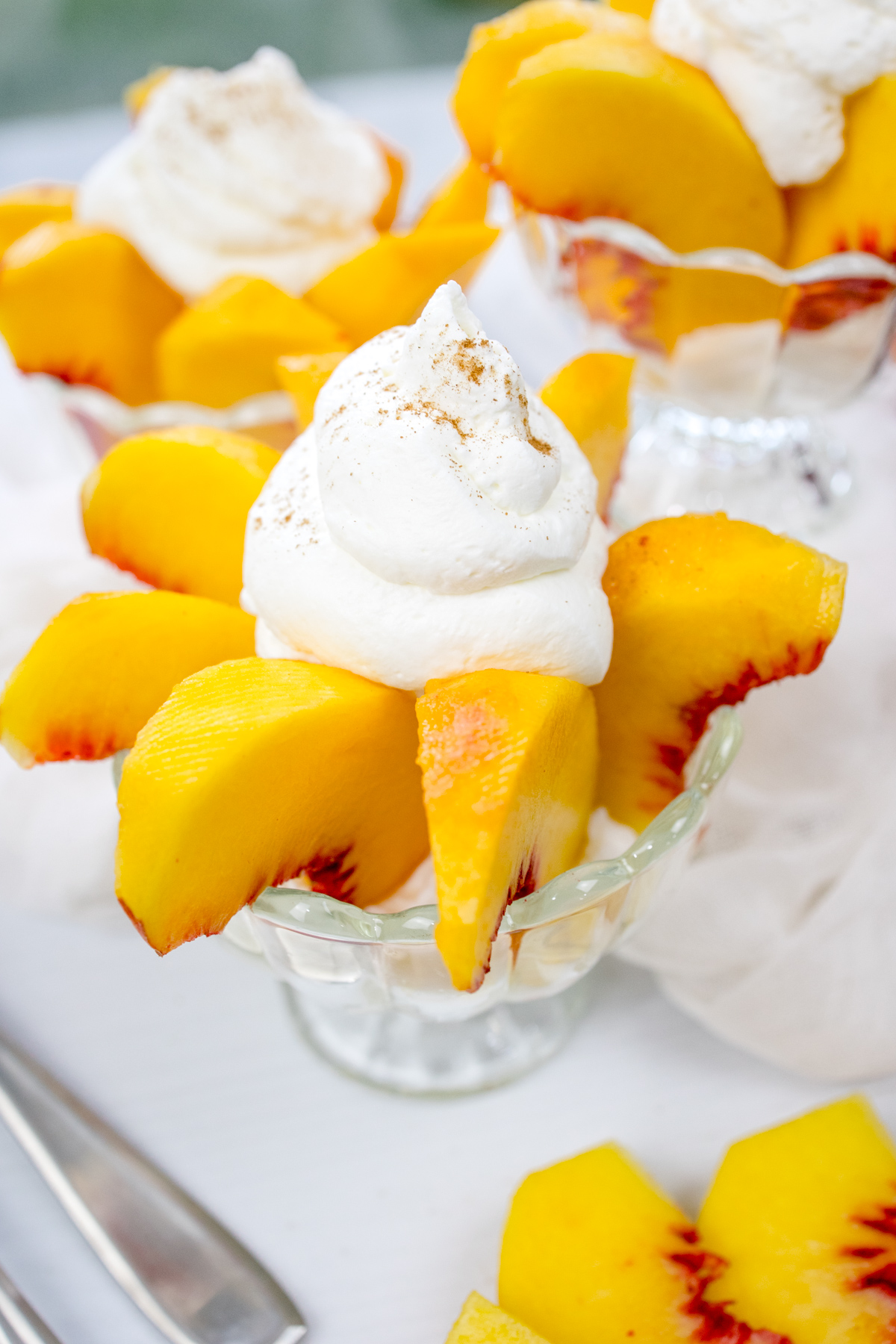 Angled view of bowls of peaches and cream surrounded by peaches and white decorations.