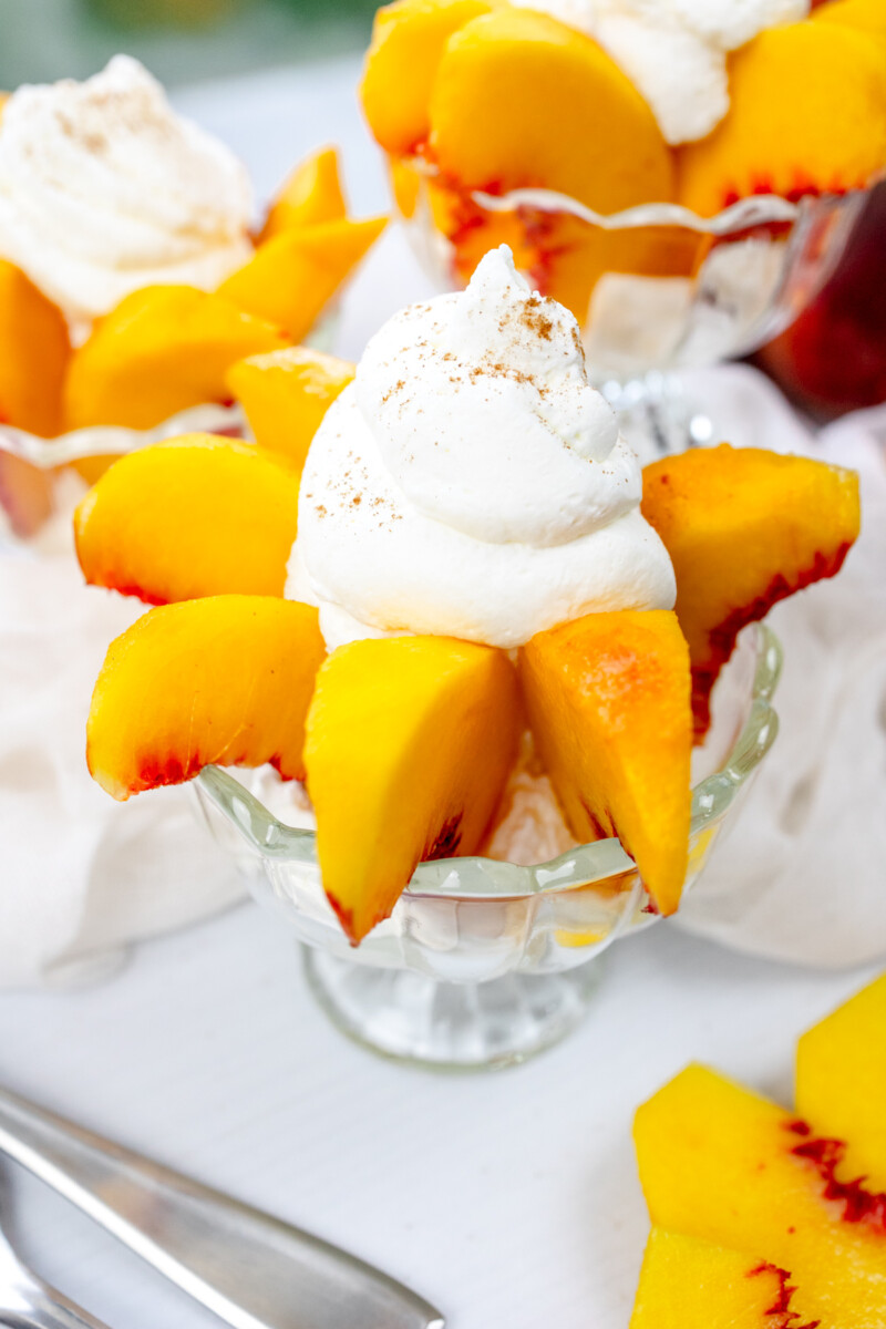 Angled view of bowls of peaches and cream surrounded by peaches and white decorations.