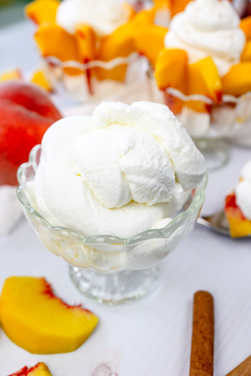 Angled view of a bowl of whipped cream with bowls of peaches and cream and peach slices around it.