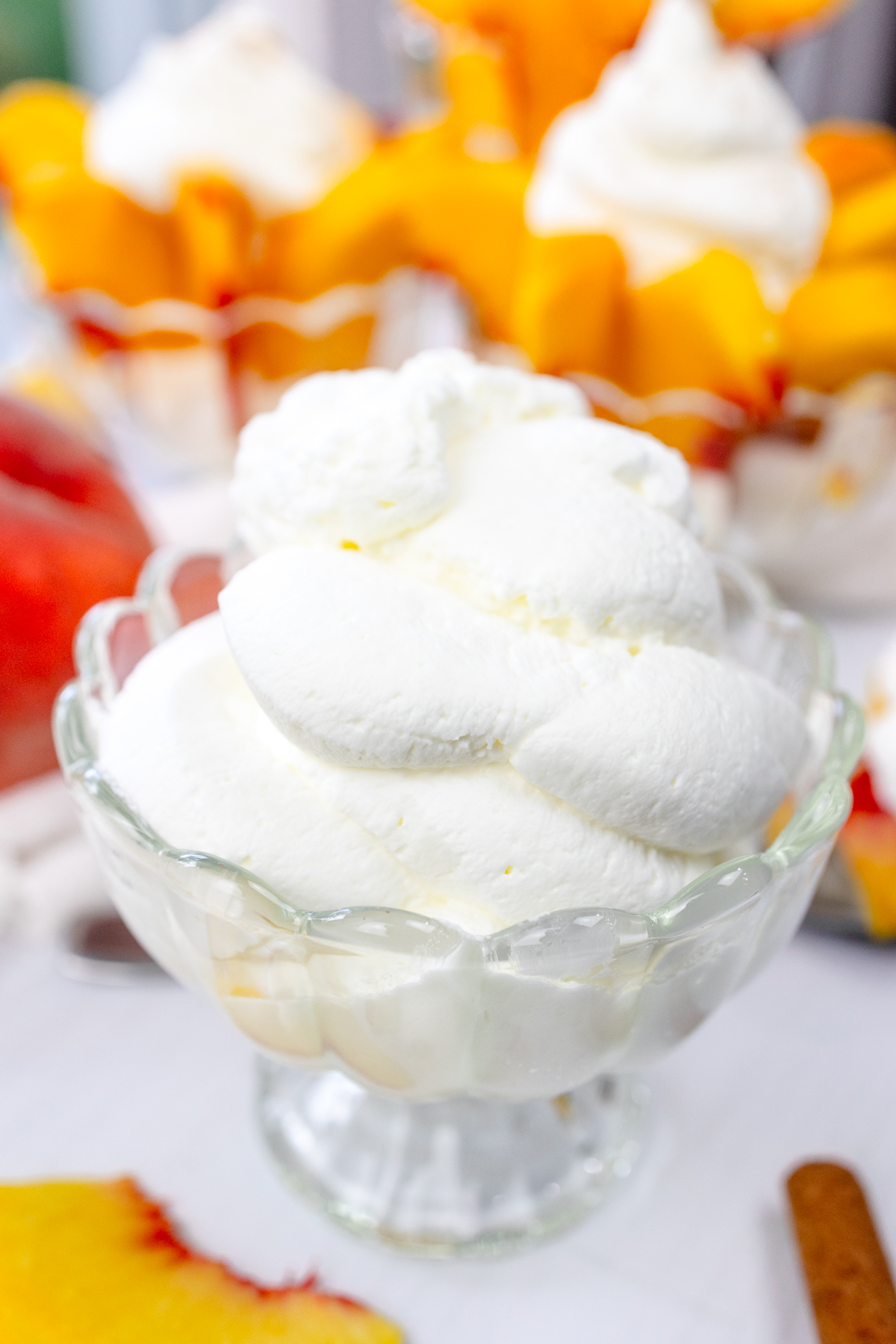 Close up view of a bowl of whipped cream with bowls of peaches and cream and peach slices around it.