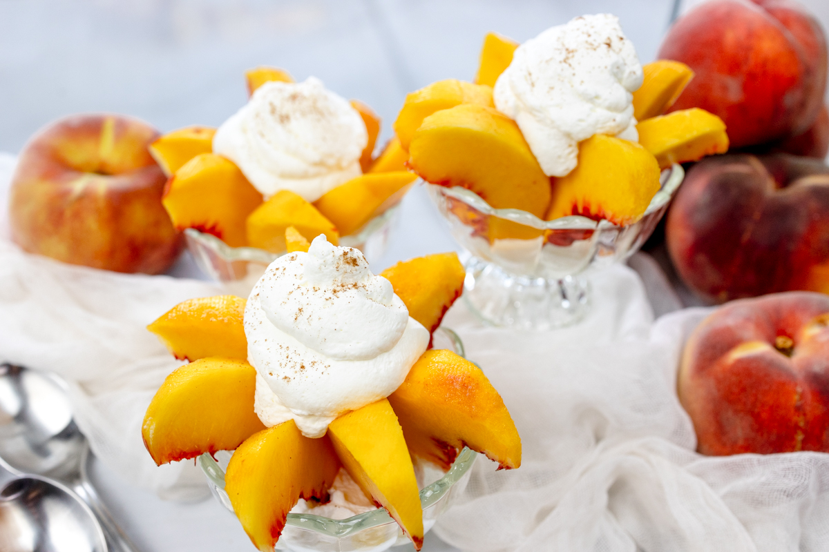 Wide view of bowls of peaches and cream surrounded by peaches and white decorations.