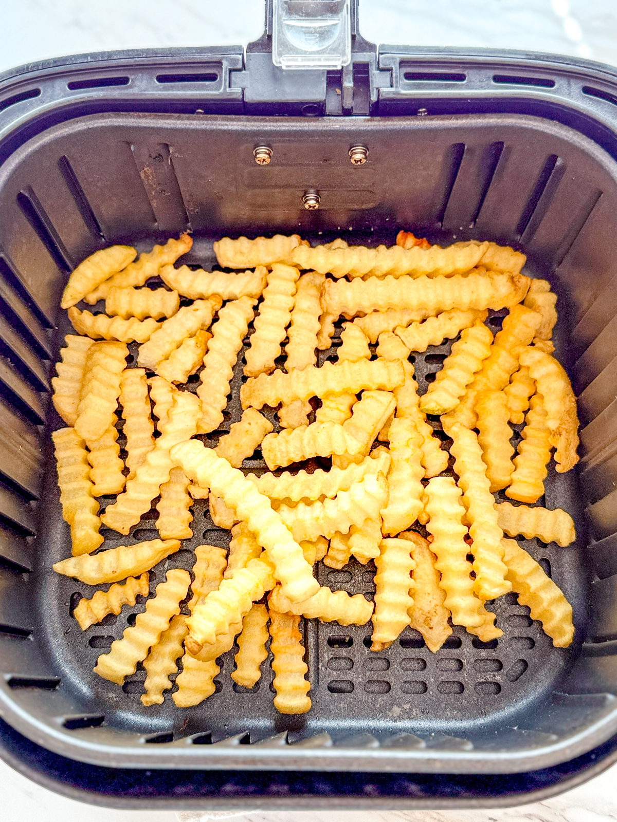 Overhead view of crinkle cut fries in an air fryer basket.