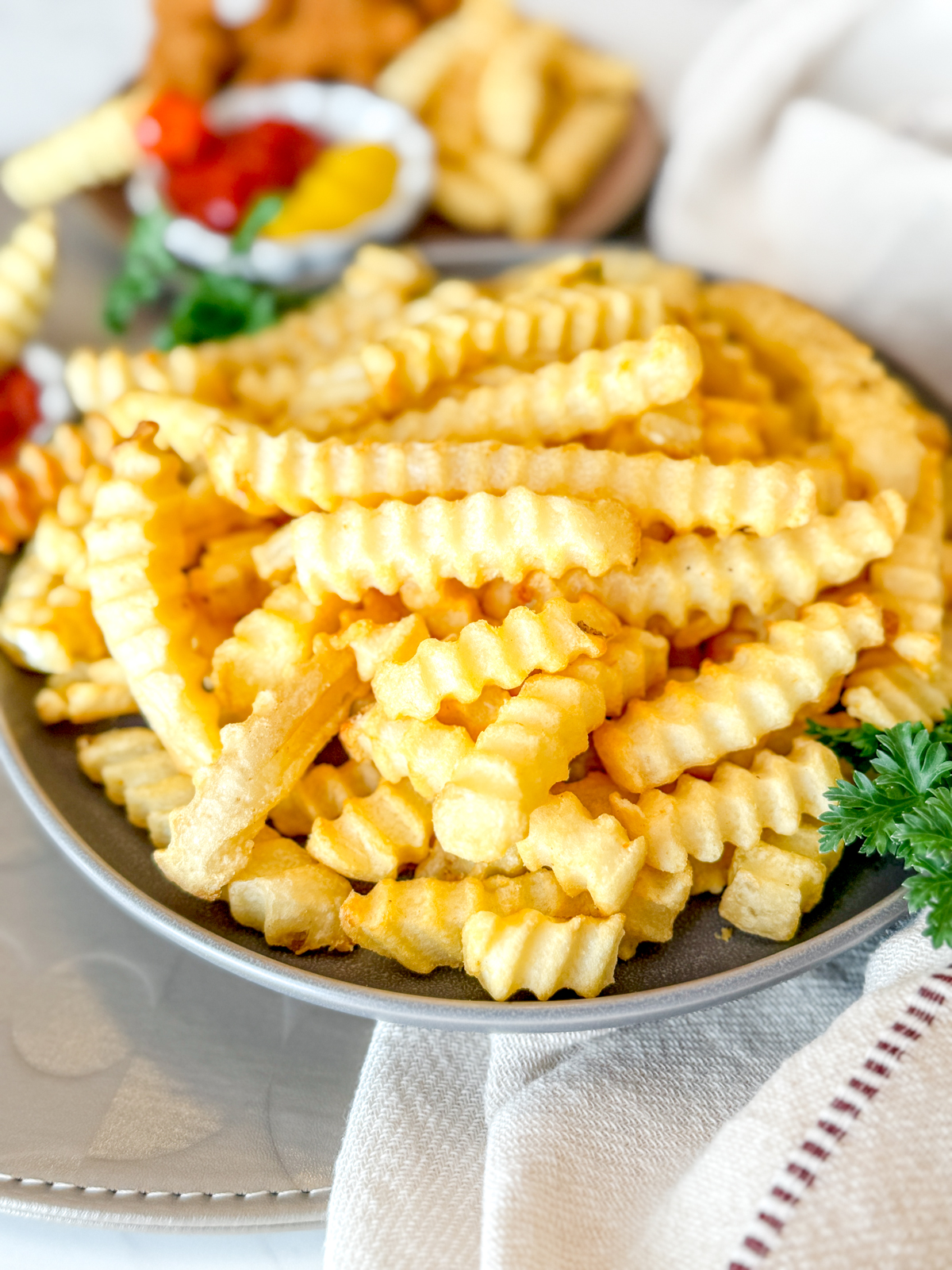 Angled view of crinkle cut fries in a bowl on a table next to dipping sauces.