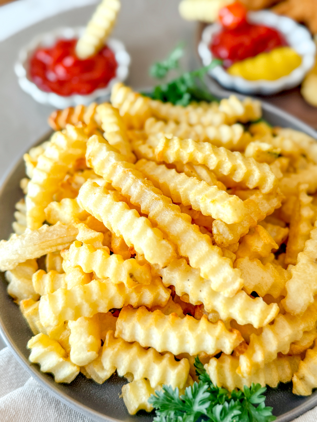 Angled view of crinkle cut fries in a bowl on a table next to dipping sauces.