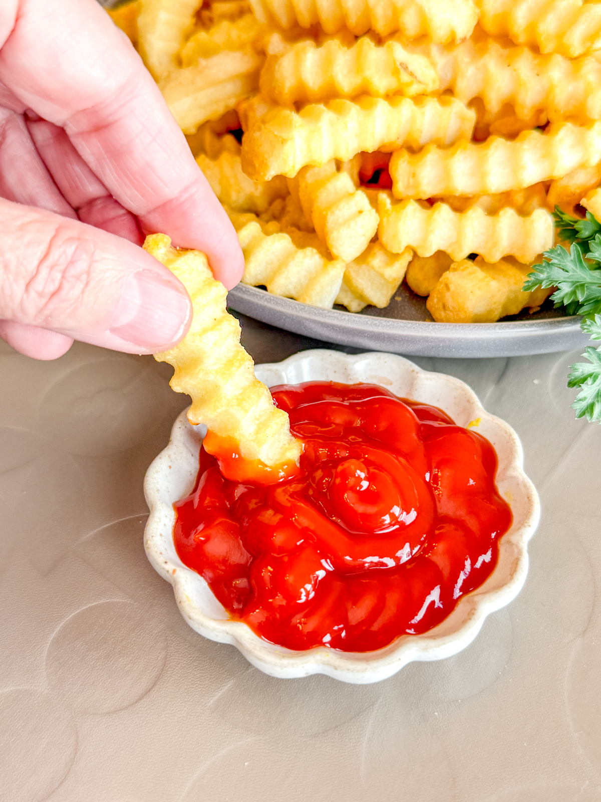 Close up view of a hand dipping a crinkle cut fry into a small bowl of ketchup.