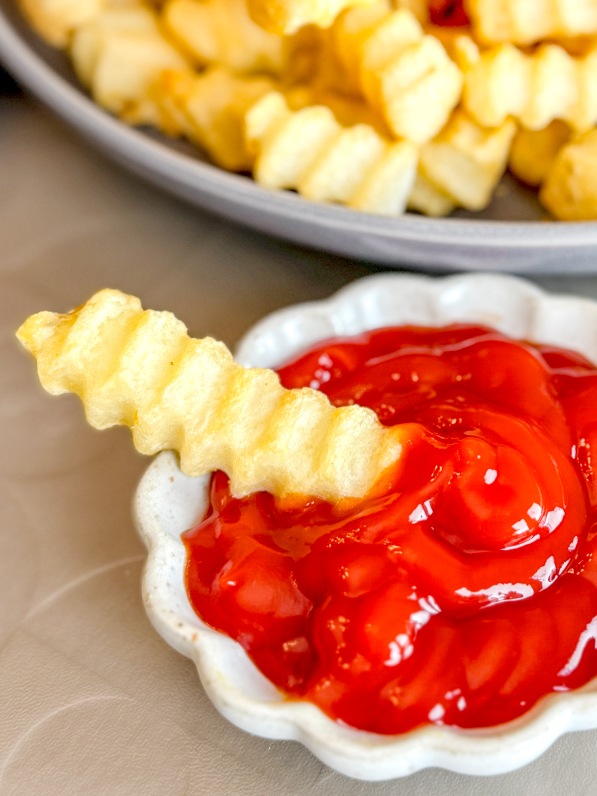 Close up view of a crinkle cut fry dipped into a small bowl of ketchup.