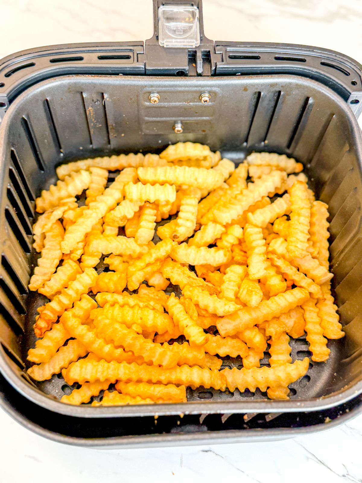 Overhead view of crinkle cut fries in an air fryer basket.