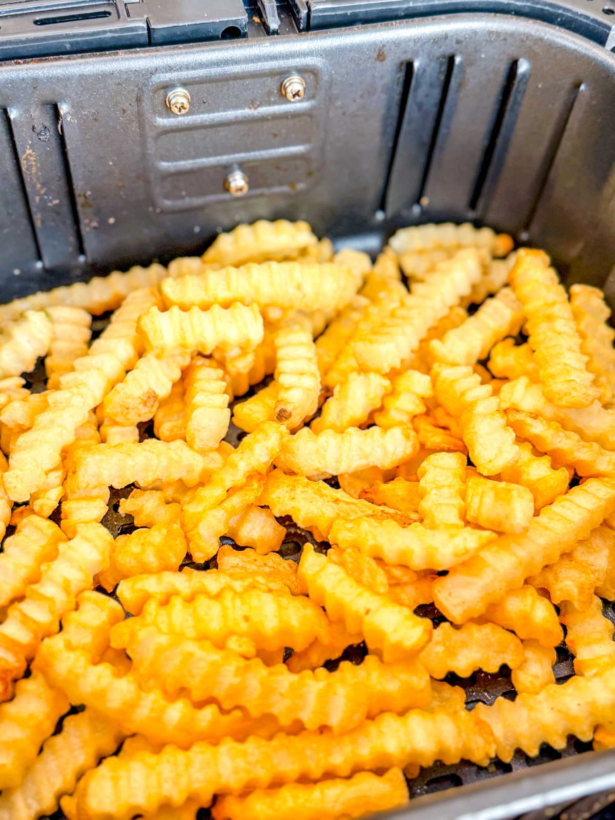 Close up view of crinkle cut fries in an air fryer basket.