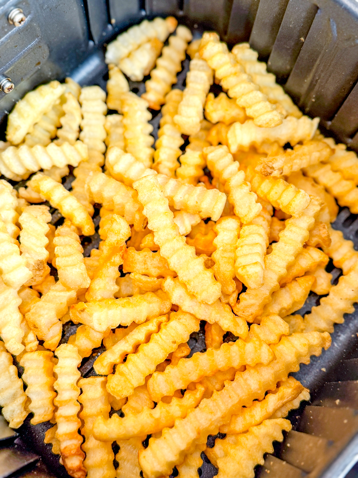 Close up view of crinkle cut fries in an air fryer basket.