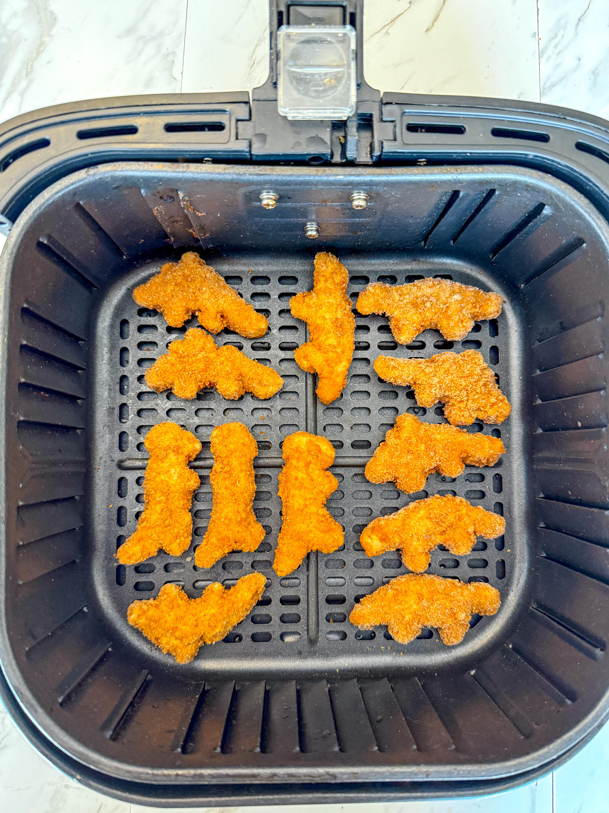 Overhead image of an air fryer basket with twelve dino nuggets in a layer on the bottom.