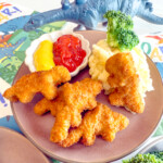 Angled view of Air Fryer Dino Nuggets on a brown plate with mashed potatoes, brocolli, and dipping sauces.