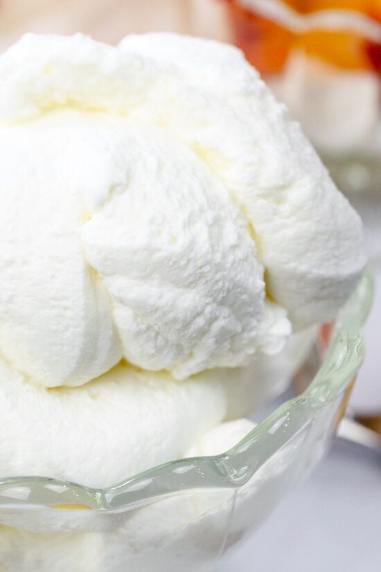 Angled view of a bowl of whipped cream with bowls of peaches and cream and peach slices around it.