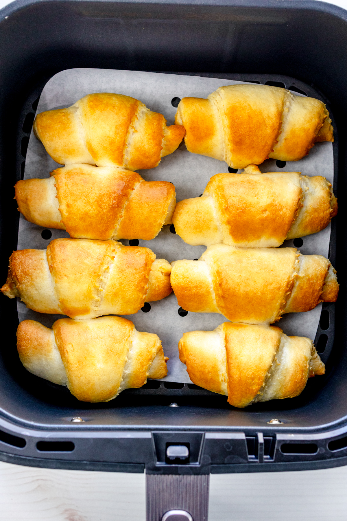 Overhead view of cooked crescent rolls in an air fryer basket.