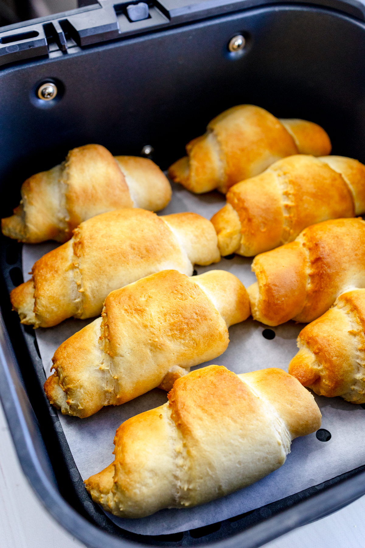 Angled view of cooked crescent rolls in an air fryer basket.