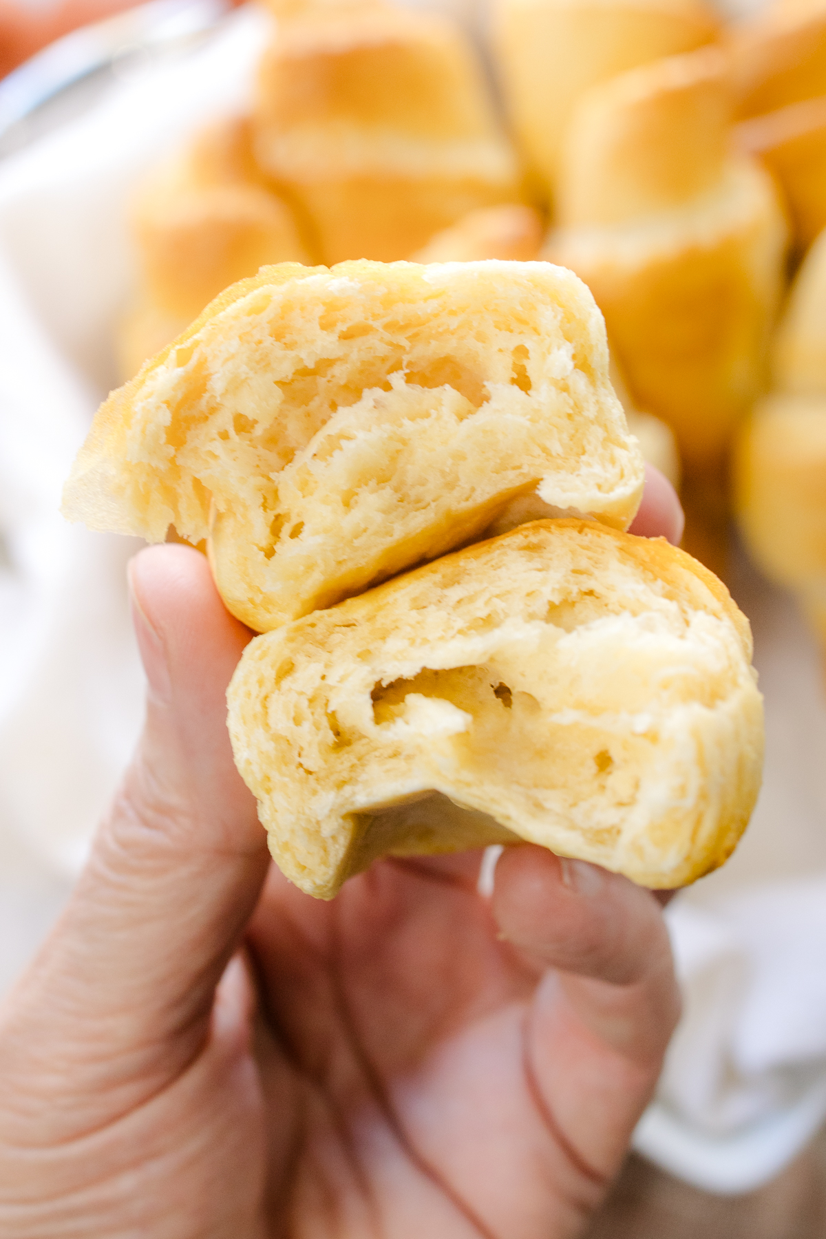 Close up view of a hand holding a crescent roll sliced in half to reveal the middle.