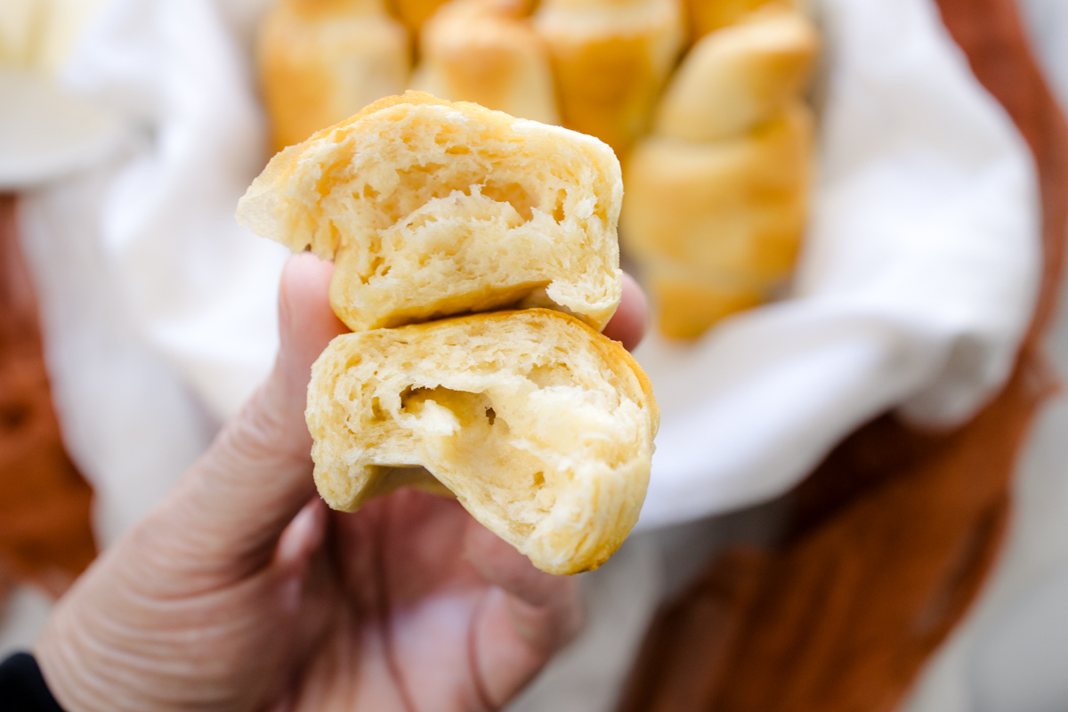 Close up view of a hand holding a crescent roll sliced in half to reveal the middle.