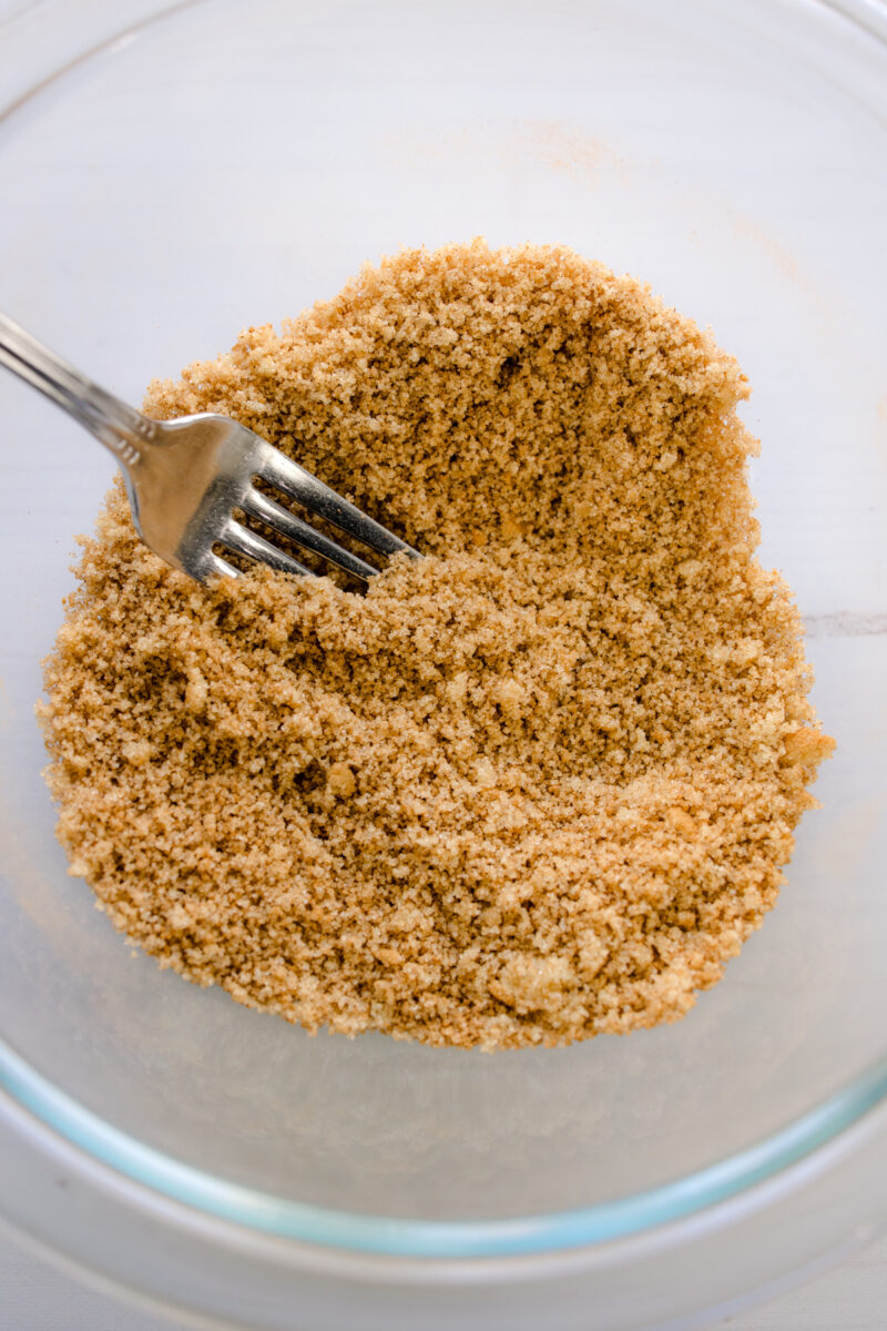 Close up overhead view of a fork mixing brown sugar and cinnamon in a glass bowl.