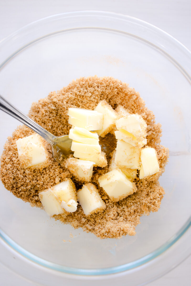 Close up overhead view of a fork mixing brown sugar, butter, and cinnamon in a glass bowl.