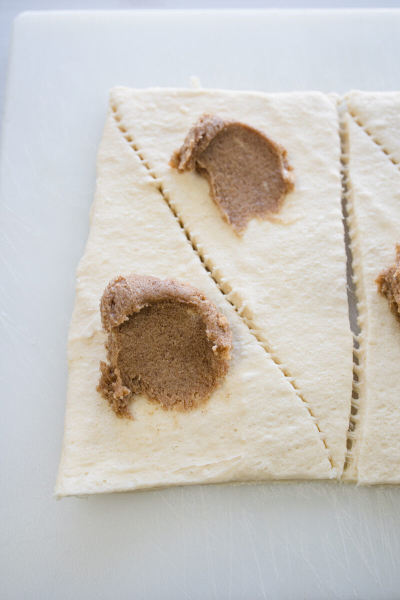 Close up view of crescent roll triangles with a dab of cinnamon-sugar-butter mixture applied.