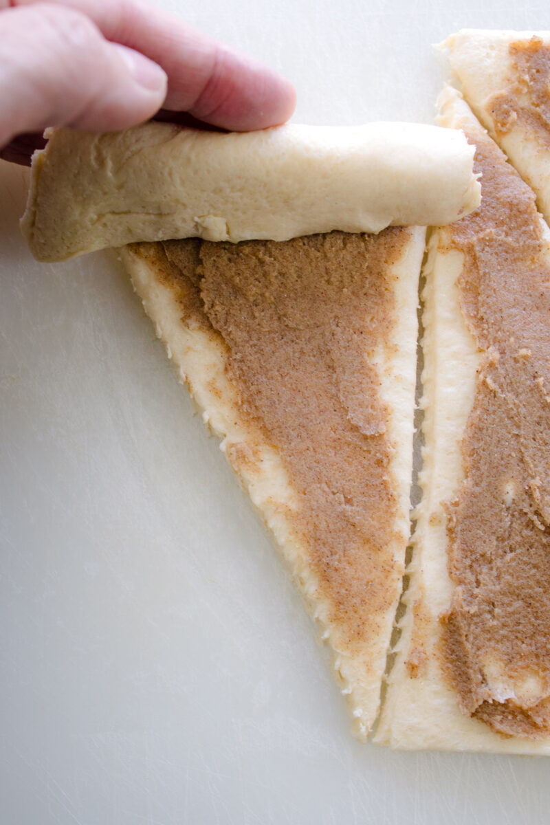Close up view of a hand rolling up a cinnamon crescent roll.