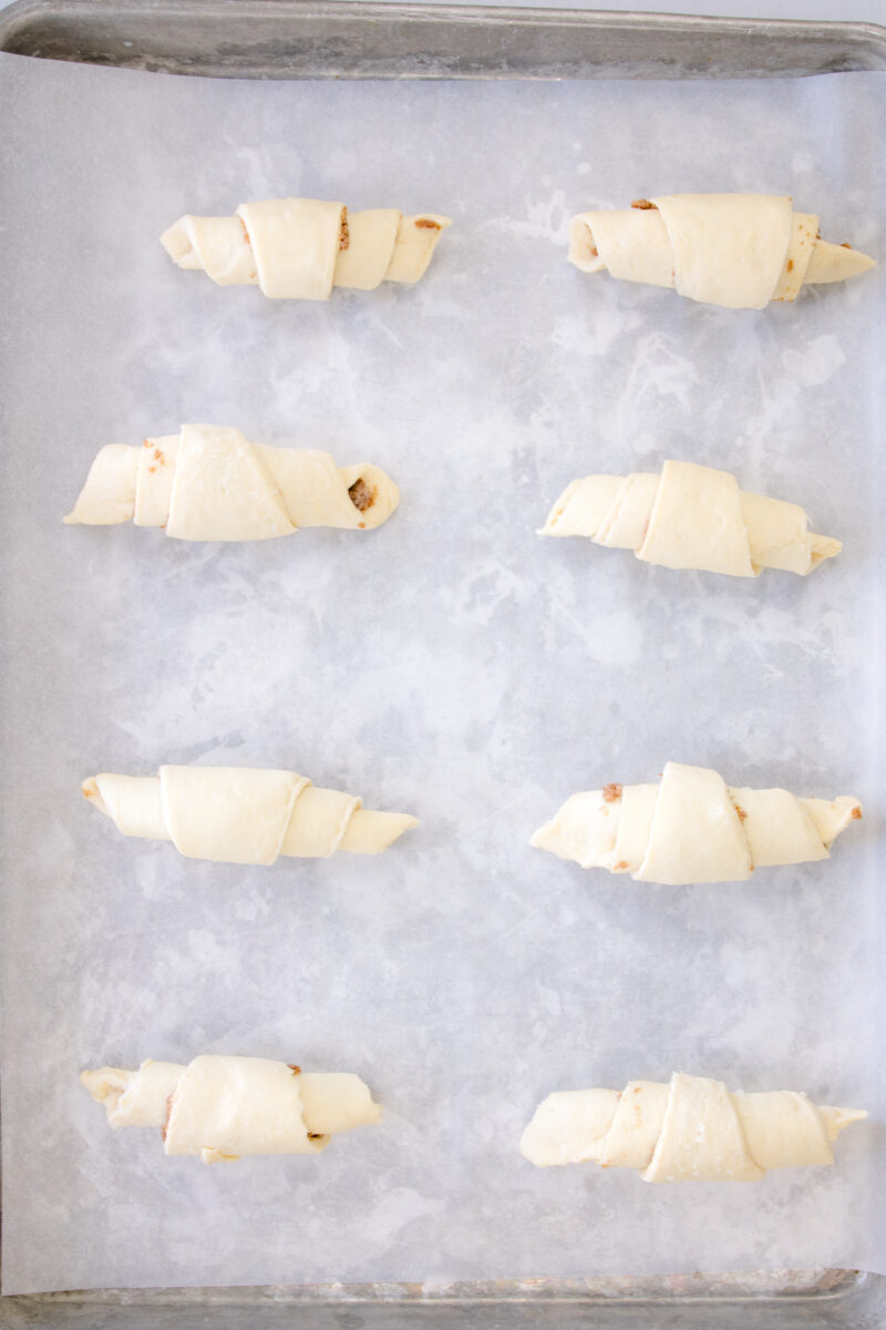 Overhead view of cinnamon crescent rolls on a baking sheet lined with parchment paper.