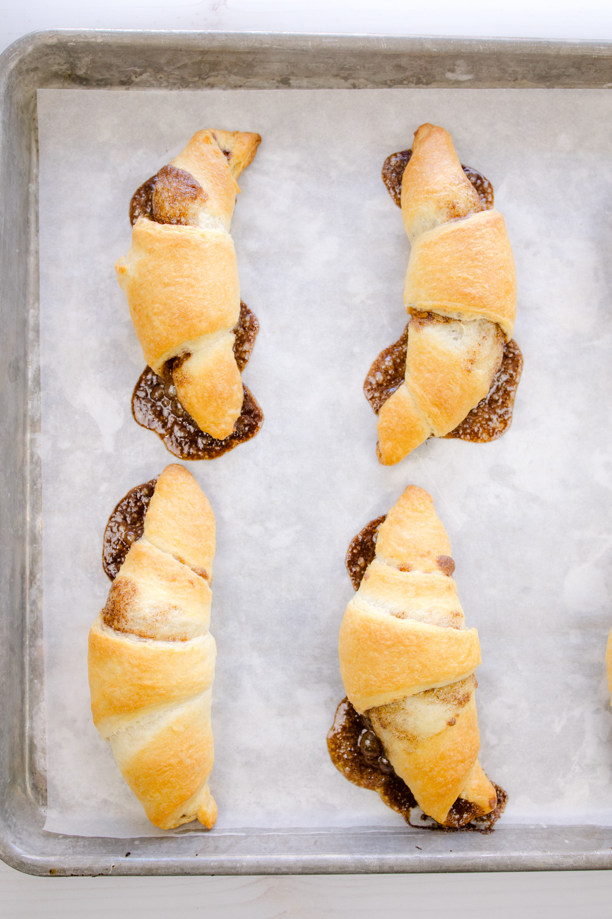 Overhead view of baked cinnamon crescent rolls on a baking sheet lined with parchment paper.